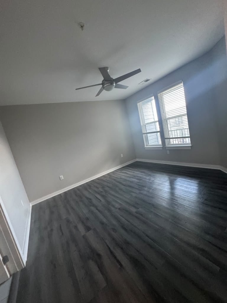 Empty bedroom with dark plank flooring, fresh walls and a ceiling fan