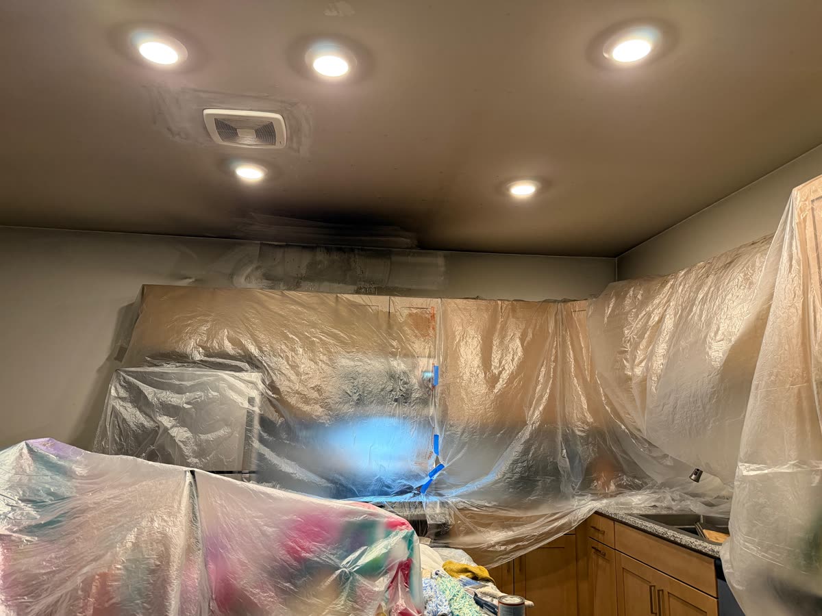 Kitchen ceiling with a dark stain above the cabinets, the room masked in plastic sheeting
