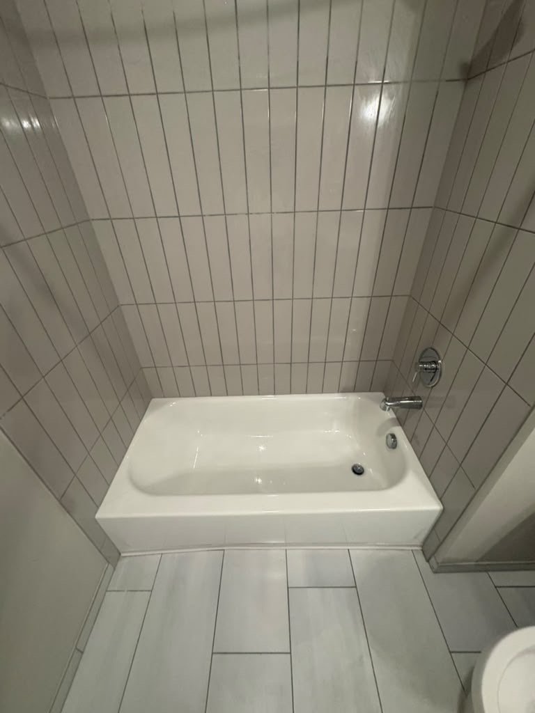 White tub with a vertical tile surround and tiled floor