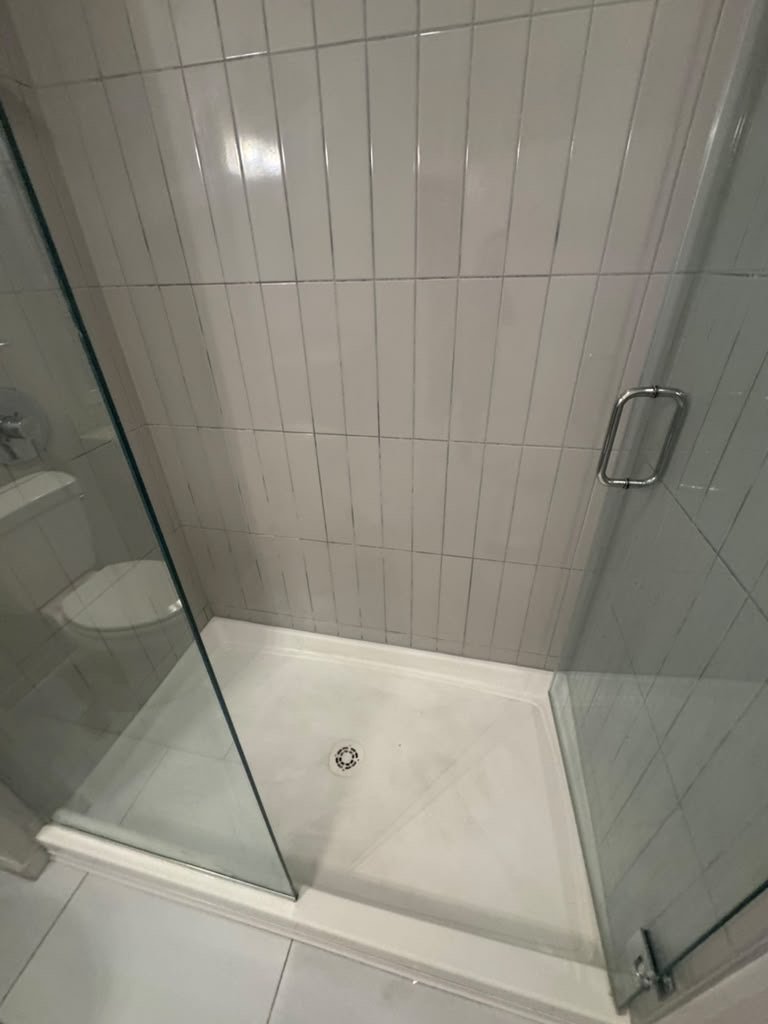 Walk-in shower with a glass door and vertical white tile