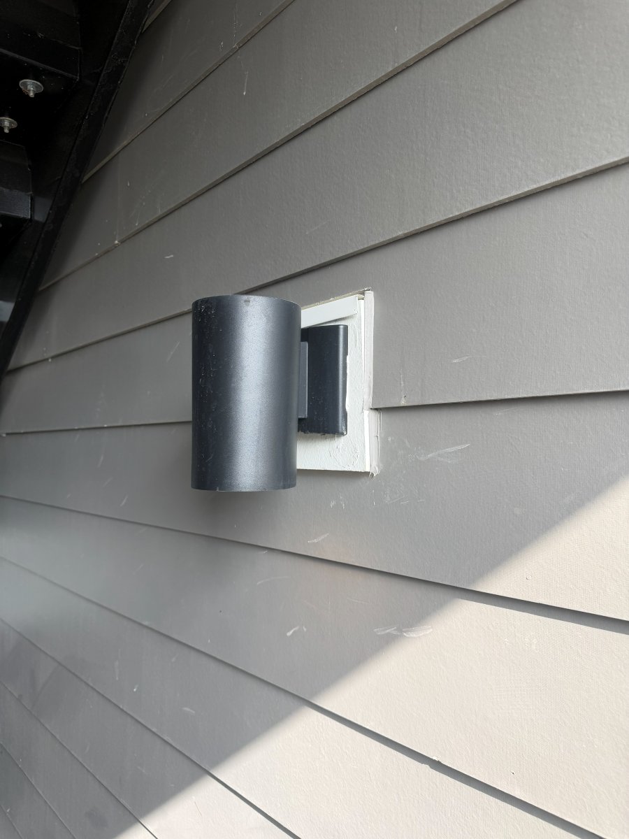 The wall light mounted flush on the siding with clean trim around it
