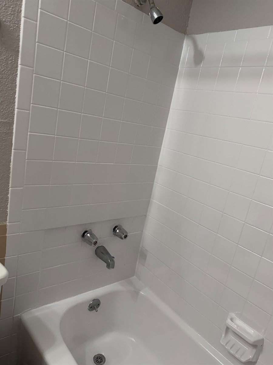Corner of a refinished tub surround showing tile and tub spout